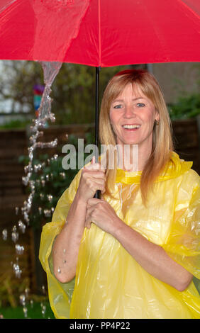 Femme portant un poncho jaune tenant un parapluie rouge sous la pluie, Banque D'Images