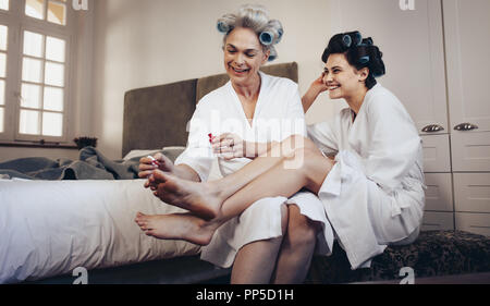 L'application de peinture à ongles mère aux pieds de sa fille à la maison. Mère et fille en peignoir avec des rouleaux sur la tête. Banque D'Images