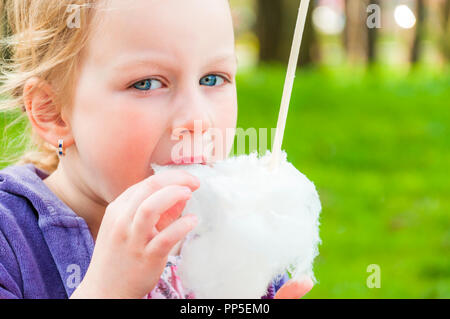 La photographie montre fille blonde aux yeux bleus que manger candy-floss bouleversée et ce qui en fait avec amour et passion pour les enfants inhérentes. Banque D'Images