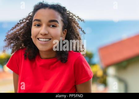 Portrait plein air de belle happy mixed race African American girl adolescent femme jeune femme souriante avec des dents parfaites et le littoral de la mer behi Banque D'Images