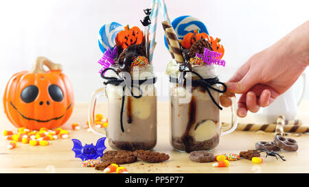 Sur-tendance Happy Halloween theme freak secoue les milk-shakes au chocolat décoré avec des bonbons, biscuits et sucettes. Banque D'Images