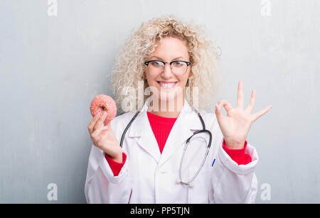 Jeune blonde dietist médecin femme de plus grunge grey wall eating ok faire signer avec les doigts, symbole excellent Banque D'Images