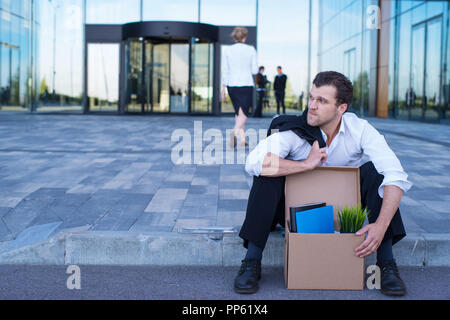 Tiré business man sitting frustré et contrarié dans la rue près de l'immeuble de bureaux de fort de ses affaires. Il a perdu travail Banque D'Images