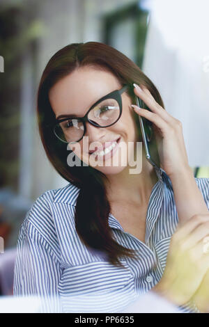 Jeune femme appelant nerd moderne confiant derrière une vitre à l'intérieur Banque D'Images