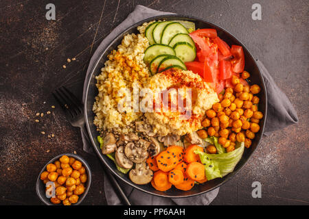 Bol Bouddha avec légumes, champignons, boulgour, pois chiches cuits et l'hummus. Fond sombre, vue du dessus. La nourriture végétalienne saine concept. Banque D'Images