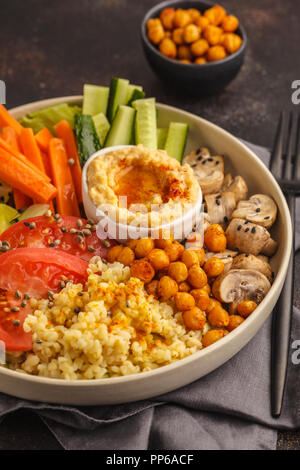 Bol Bouddha avec légumes, champignons, boulgour, pois chiches cuits et l'hummus. Fond sombre.Healthy vegan food concept. Banque D'Images