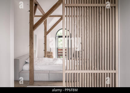 Chambre à coucher moderne avec des murs blancs, du parquet, de poutres apparentes et d'une partition du réseau. Il y a un lit avec des draps gris lumière, les portes d'un balcon, de coffres Banque D'Images