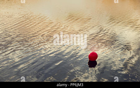 La bouée rouge marquant la zone de baignade, avec le reflet du coucher de soleil sur l'eau Banque D'Images