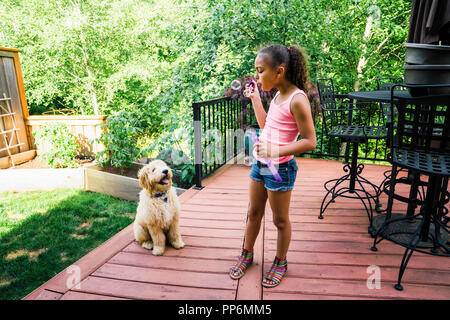 Le Tween Girl Blowing Bubbles avec Labradoodle Puppy in Backyard Banque D'Images