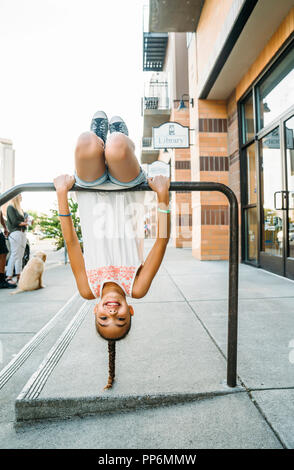 Heureux, smiling girl hanging from porte vélo bar on sidewalk Banque D'Images