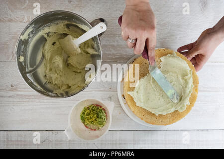 Un gin tonic glacé aromatisé cake maison en cours, une main avec un couteau à palette, le givrage de lissage et un bol de glace fraîche et de zeste de citron. Banque D'Images