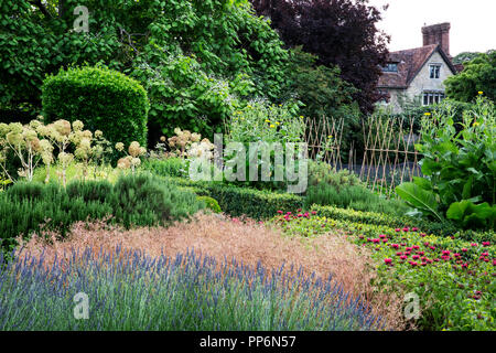 Jardin clos avec parterres de fleurs, arbustes et arbres, manoir historique dans l'arrière-plan. Banque D'Images