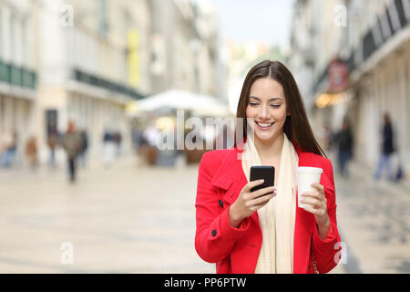 Vue avant portrait of a happy lady walking in the street en utilisant un téléphone intelligent en hiver avec copie espace à côté Banque D'Images