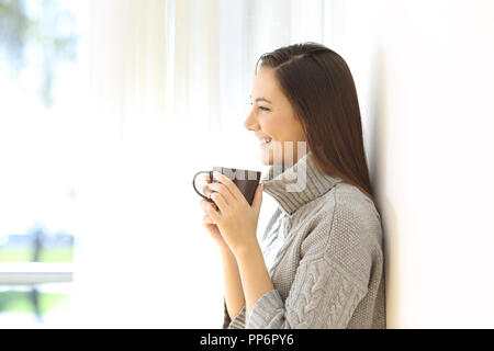 Profil d'une femme tenant une tasse à café debout à la maison en hiver Banque D'Images