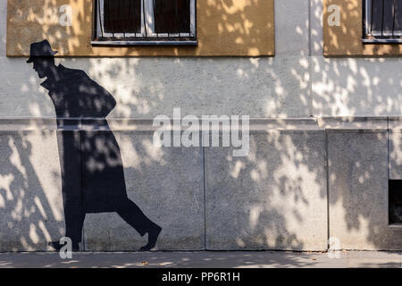 Fragment de la façade de la maison avec la peinture noire de l'homme marche dans le manteau représenté sur le mur. Banque D'Images