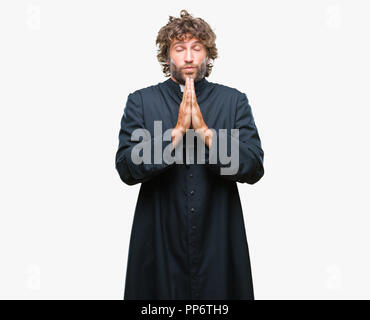 Beau prêtre catholique hispanique homme sur fond isolé en prière avec les mains pour lui demander pardon sourire confiant. Banque D'Images