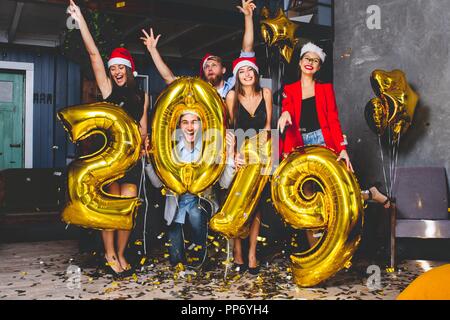 La célébration de la célébration du Nouvel An. Groupe de cheerful young in belle portant les numéros 2019 de l'or et du lancer de confettis. Banque D'Images