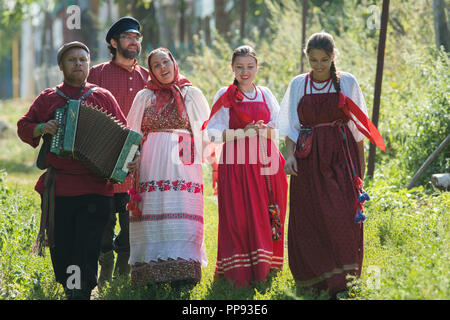 Groupe d'hommes et femmes en costumes folkloriques russes dans la nature. L'homme joue de l'accordéon. Célébration Banque D'Images