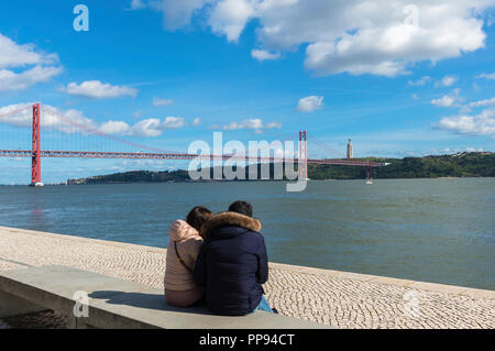 Jeune couple assis sur le fleuve Tage et regardant le 25 avril Pont sur le Tage, Lisbonne, Portugal Banque D'Images