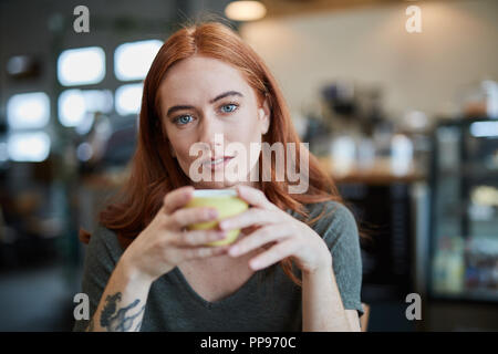 Une seule femelle, est assis dans un café de la ville avec une boisson chaude dans une tasse, looking at camera Banque D'Images