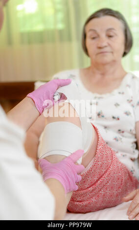 Bandages médecin senior woman jambe à la maison. Médecin de l'administration des premiers soins au patient. L'accent est mis sur la main du médecin. Banque D'Images