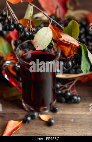 Des jus de fruits noirs mûrs (chokeberry Aronia melanocarpa) dans du verre et de petits fruits avec des feuilles sur fond de bois. Banque D'Images