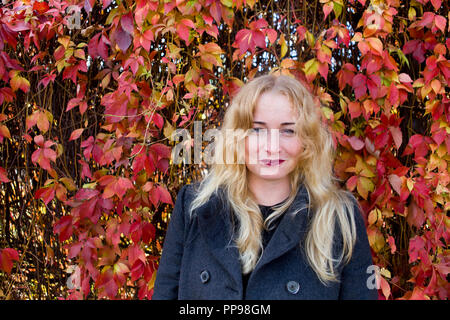 Femme blonde debout près de clôture à partir des feuilles, essayant de contenir ses émotions Banque D'Images