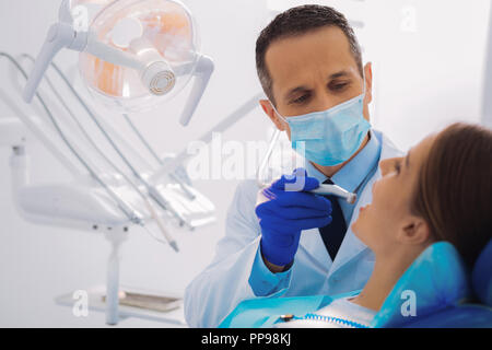 Médecin sérieux tenant une fraise dentaire en durcissant sous l'effet de son patient Banque D'Images