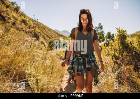 Jeune femme marche sur un sentier de montagne avec des amis à l'arrière. Femelle avec les amis de la randonnée sur un chemin de terre dans un pays. Banque D'Images