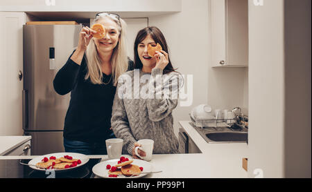 Happy mother and daughter standing dans la cuisine avec plaques plein de cookies. Deux smiling women in kitchen holding cookies devant leurs yeux. Banque D'Images