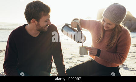 Belle jeune couple having coffee à la plage. Woman pouring coffee dans une tasse pour l'homme à la mer. Banque D'Images