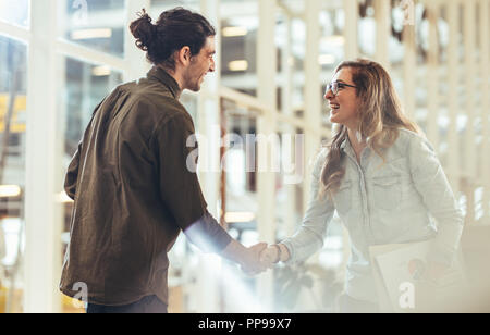 Des collègues d'affaires heureux chaque message d'autres en se serrant la main au lieu de travail. Les papiers du bureau comptable Businesswoman shaking hand avec un collea Banque D'Images