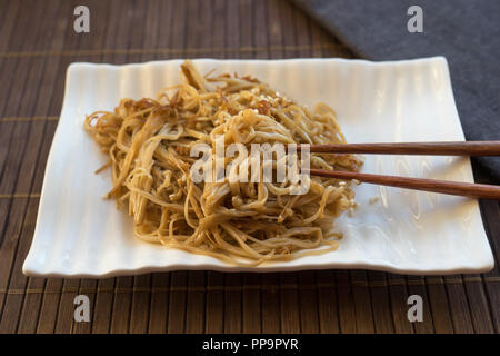 Poêlée de champignons enoke dans la sauce de soja sur une assiette blanche. La nourriture asiatique Banque D'Images