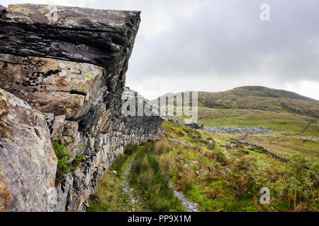 Mur en surplomb au-dessus de vieilles lignes de tram dans Gorseddau ardoise avec Moel Ddu au-delà dans le parc national de Snowdonia. Cwmystradllyn Gwynedd au Pays de Galles UK Banque D'Images