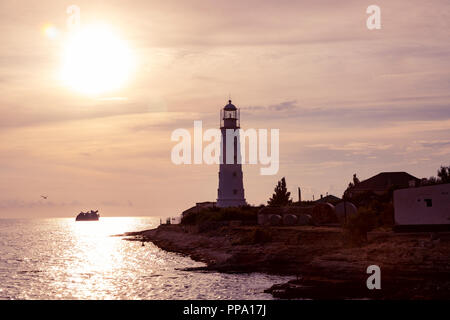 Faisceau du projecteur phare près de l'océan au coucher du soleil. Phare au coucher du soleil au crépuscule par temps clair Banque D'Images