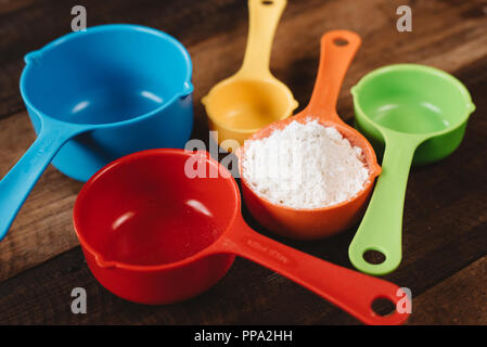 Tasses à mesurer colorés avec de la farine sur la table en bois. Concept de la cuisine et outils de cuisine Banque D'Images