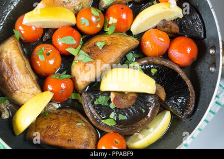 Les champignons et tomates cerises sautées étant dans une poêle peu profonde, garnie de persil frais haché et des quartiers de citron Banque D'Images