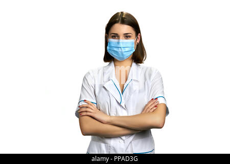 Femme médecin au masque de visage sur fond blanc. Belle femme médecin avec les bras croisés, portrait. Banque D'Images