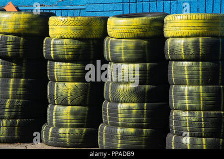 Des piles de vieux pneus (pneus) avec peinture jaune sur l'extérieur d'un centre de pneus Banque D'Images