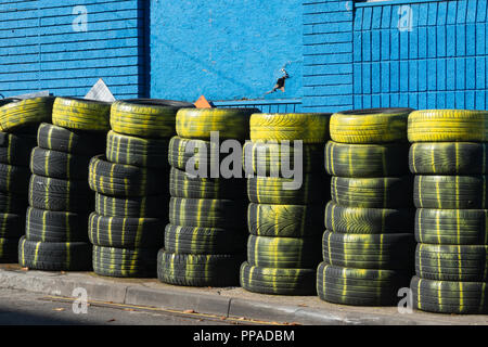 Des piles de vieux pneus (pneus) avec peinture jaune sur l'extérieur d'un centre de pneus Banque D'Images