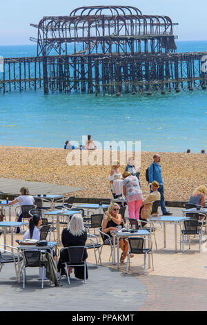 Des gens assis sur le trottoir devant un café sur le front de mer de Brighton, East Sussex. Dans l'arrière-plan est l'incendié jetée victorienne. Banque D'Images