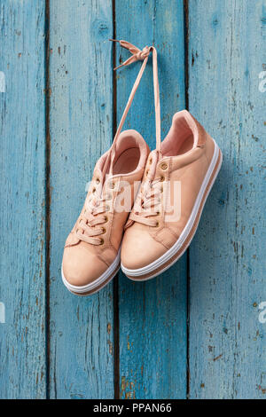 Paire de chaussures de sport femme beige accroché sur une corde sur un fond d'un vieux mur en bois bleu Banque D'Images