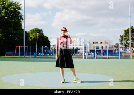 Fashion shoot avec une fille portant un haut marron et une jupe noire dans un parc de basket-ball Banque D'Images