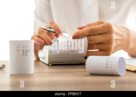 Femme faire ses calculs sur une calculatrice ou d'une calculatrice de l'extraction de rames de papier avec des chiffres imprimés et totaux, conceptuel de la comptabilité a boo Banque D'Images