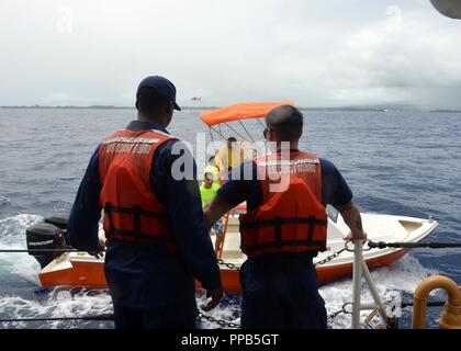 Une intervention des pompiers Hawaii Comté d'équipage de bateau s'arrête à côté de la Coast Guard Cutter Oliver Berry (WPC 1124) tandis qu'une station d'Air Point MH-65 barbiers de l'équipage de l'hélicoptère Dauphin plane dans le fond près de Hilo, Hawaii, le 15 août 2018. La Garde côtière et Hawaii Comté effectuaient un exercice de recherche et sauvetage pour augmenter l'efficacité de l'interagence. Banque D'Images