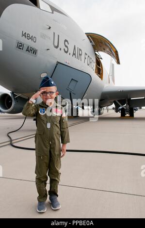 L'Armée de l'air Colonel honoraire Shane Sagraves présente un salut, tandis que l'aviateur d'un KC-135 Stratotanker affecté à la 121e Escadre de ravitaillement en vol effectue des vérifications avant vol sur la piste à la base de la Garde nationale aérienne Rickenbacker à Columbus, Ohio le 22 août 2018. Shane et le reste de sa famille ont été accueillis par le 121e ARW pour "Pilote d'un jour", qui donne pour enfants et adolescents avec une maladie chronique ou une maladie qui menace leur vie la possibilité de vivre une journée dans la vie d'une garde nationale aérienne. Shane's busy day comprenait une visite du KC-135 Stratotanker, la formation dans le simulateur de ravitaillement en vol, et un Banque D'Images