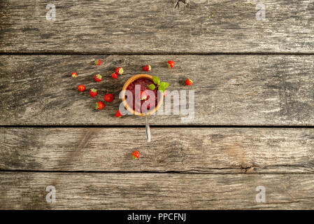 Vue de dessus de la confiture de fraise faite maison délicieux servi dans un bol en bois décoré de feuilles de menthe fraîche et de fraise mûre, éparpillés autour de Banque D'Images