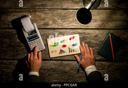 Vue de dessus d'un homme à l'aide de calculatrice avec impression en sortant avec un bloc-notes plein de graphiques en couleur, des graphiques et des chiffres en face de lui et un crayon en t Banque D'Images