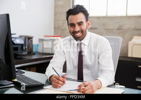 Young Hispanic male professional at desk smiling to camera Banque D'Images