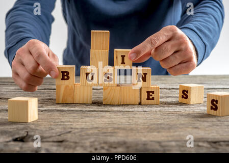 Close up de la main d'un homme d'affaires le mot de construction avec des blocs de bois sur une table rustique dans une image conceptuelle. Banque D'Images